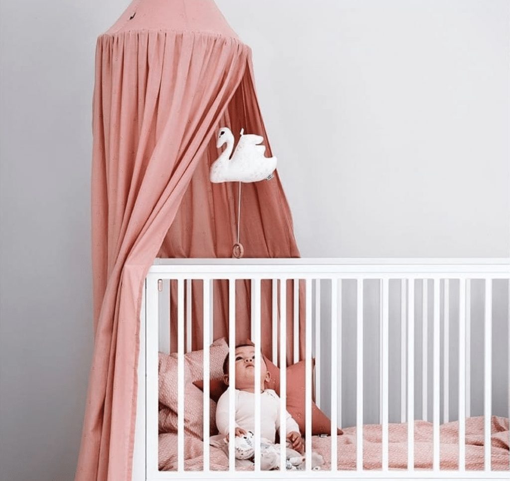 Baby canopy old rose over cot with baby and swan mobile