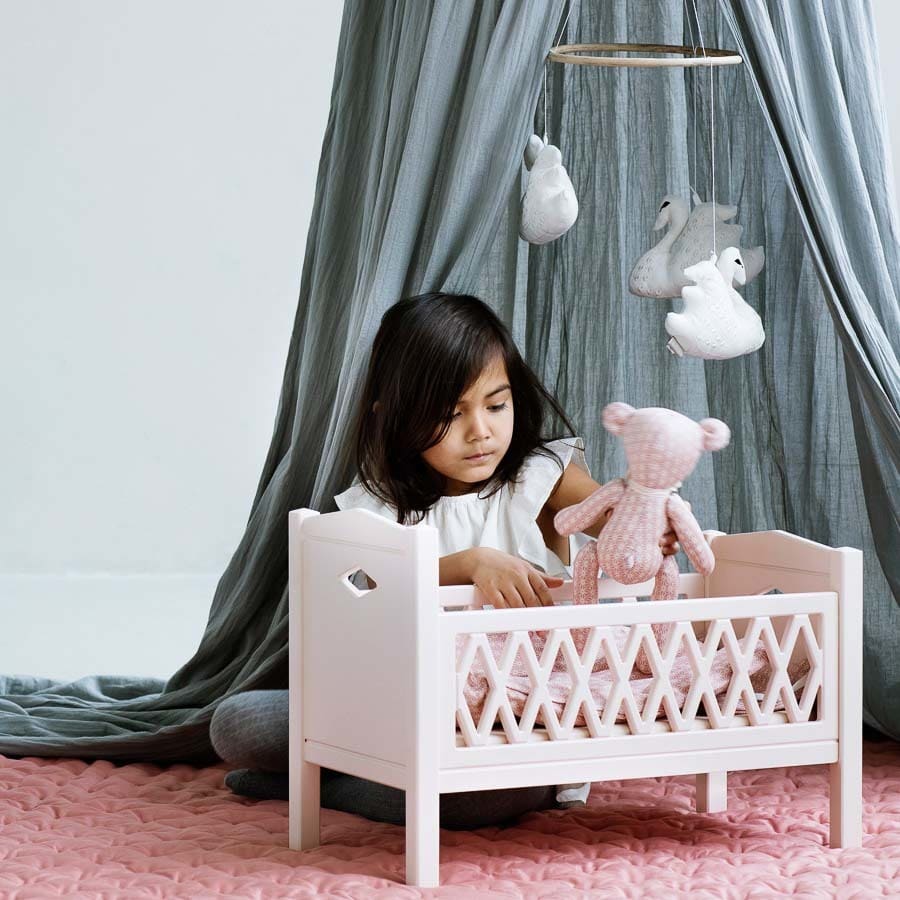 Child in nursery playing with harlequin dolls bed in rose
