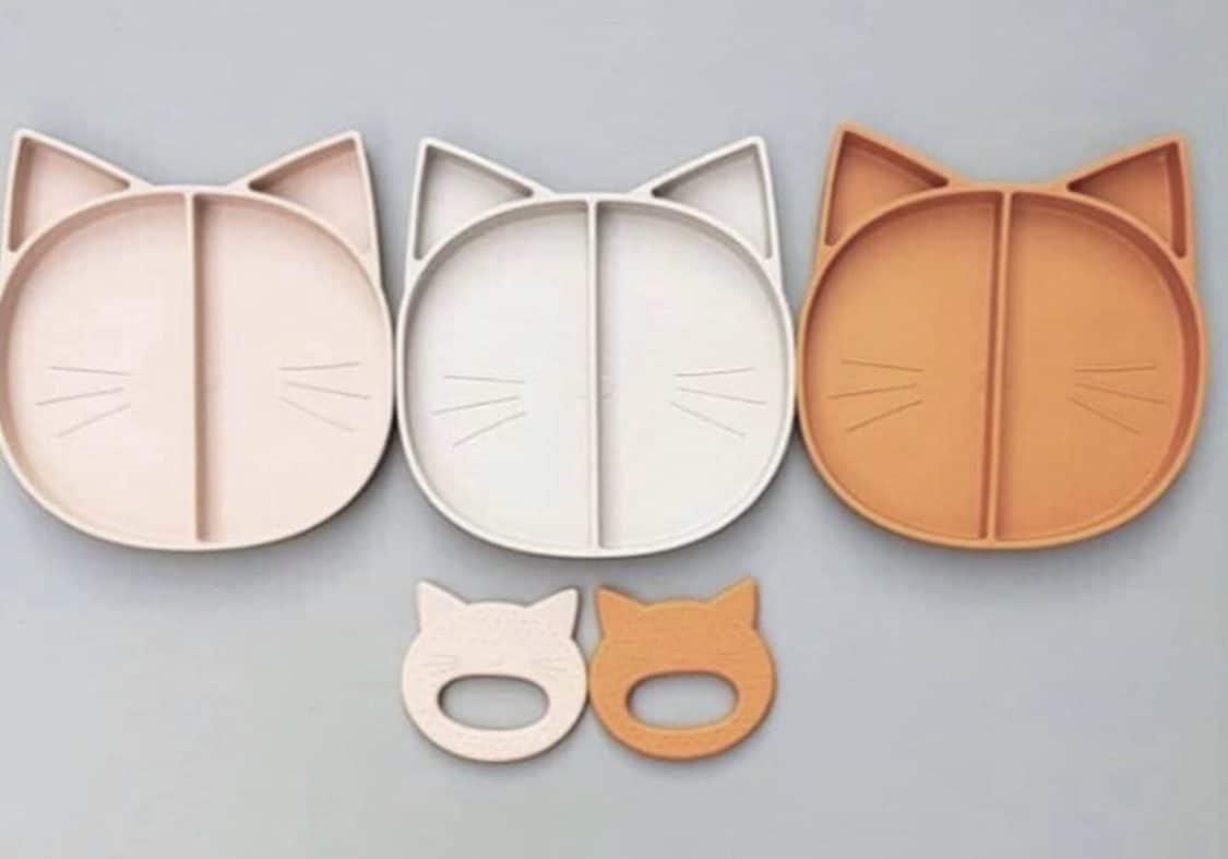 Three cat shaped silicone divided plates lined up with two cat shaped silicone baby teether underneath them