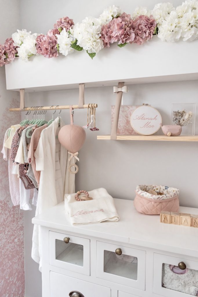 Baby nursery with white changing table, pink balloon music mobile, storage basket and wooden teething ring on display